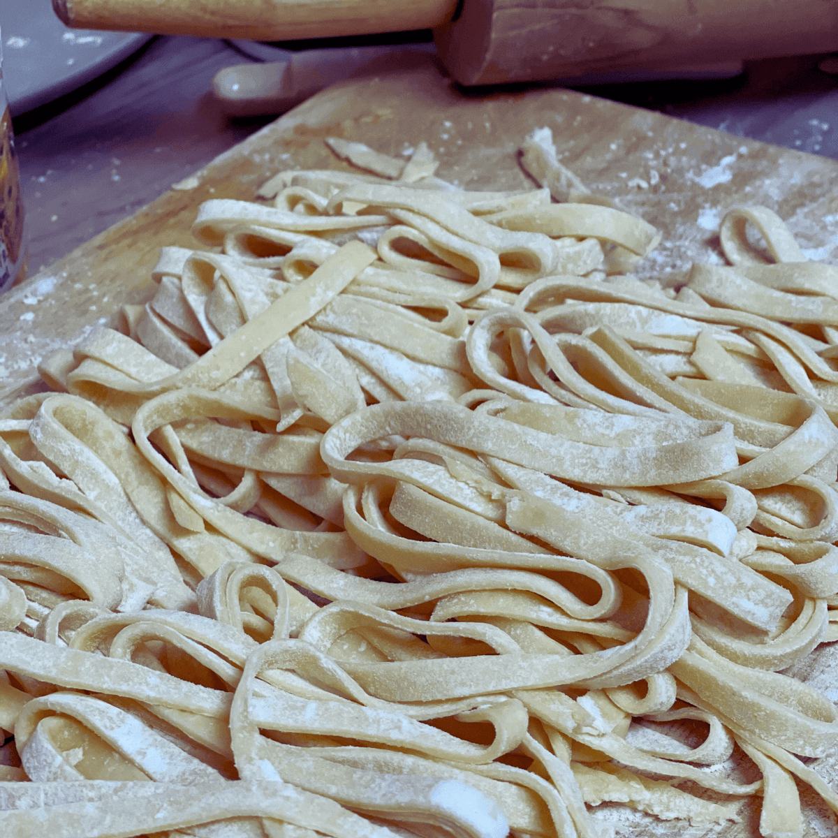 Fresh egg noodles laying on wood cutting board with flour dusted on top. 