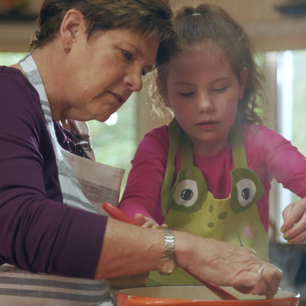 Grandmother and granddaughter cooking chicken noodle soup together. 