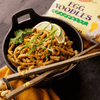 Egg noodles covered in creamy peanut sauce plated in a bowl with lime and cilantro as garnish. 
