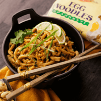 Egg noodles covered in creamy peanut sauce plated in a bowl with lime and cilantro as garnish. 