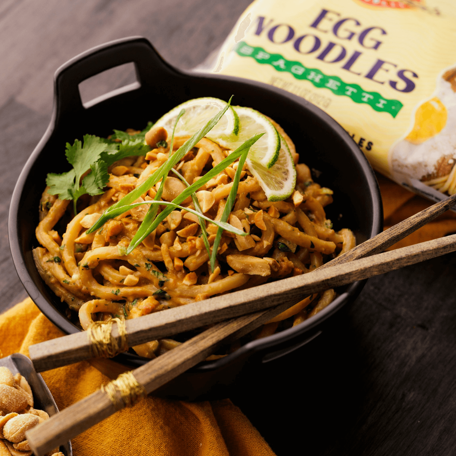 Egg noodles covered in creamy peanut sauce plated in a bowl with lime and cilantro as garnish. 