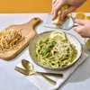 Fresh pesto and egg noodles plated with parmesan cheese getting grated on top. 