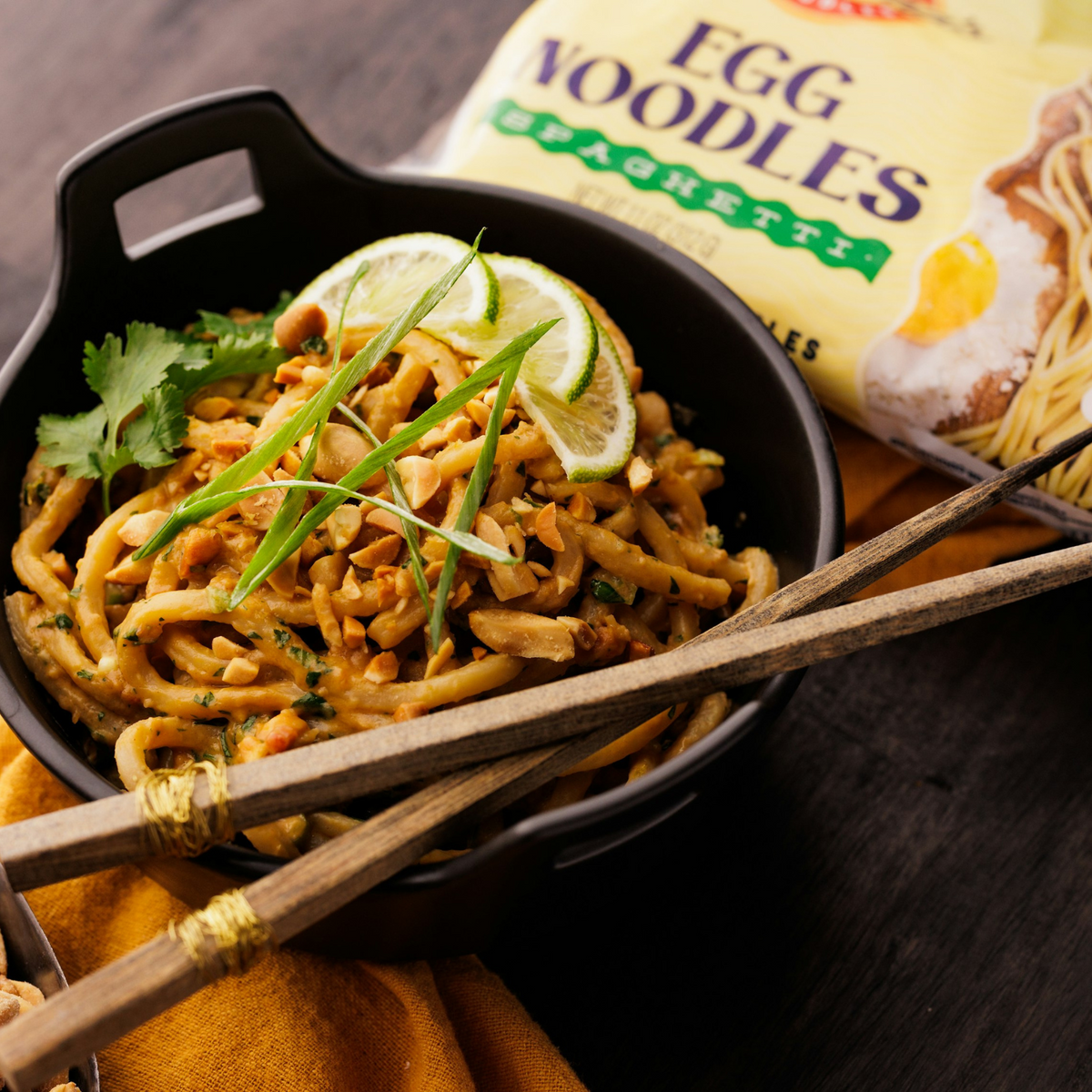 Egg noodles covered in creamy peanut sauce plated with chopsticks and fresh lime garnish on top. 