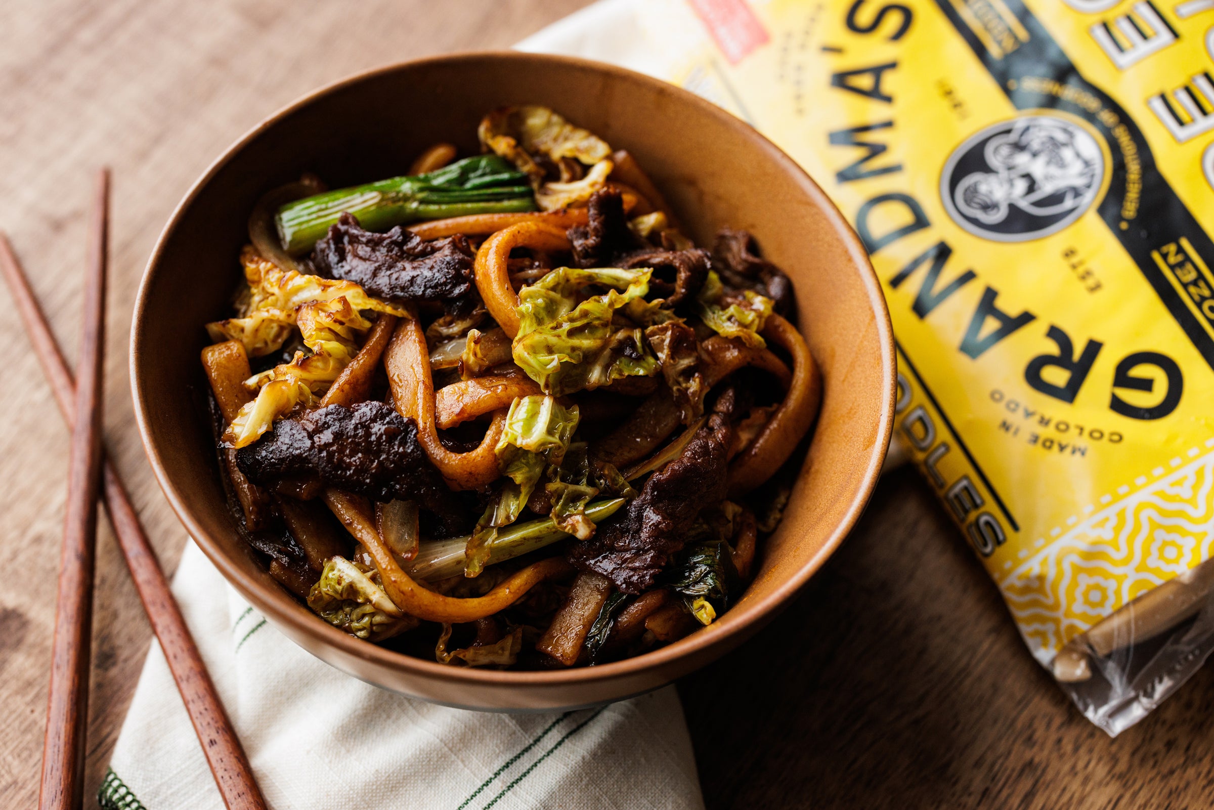 Bowl of stir fry noodles with grandma's noodles packaging placed in background. 